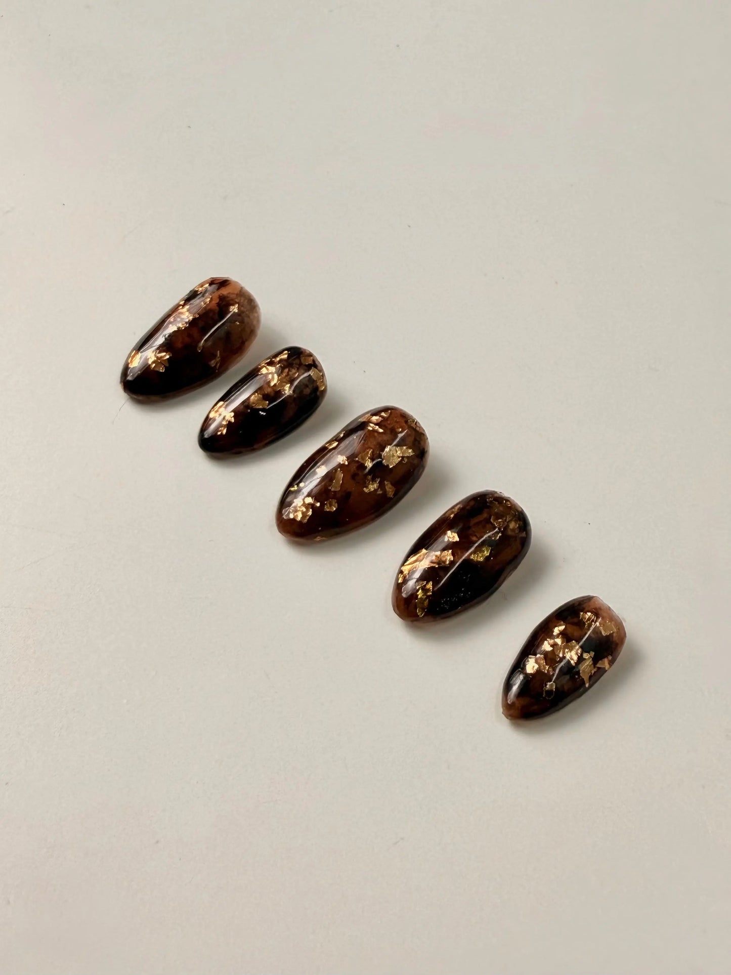 5 press on nails designed in tortoise shell with gold flakes sit in a neat line