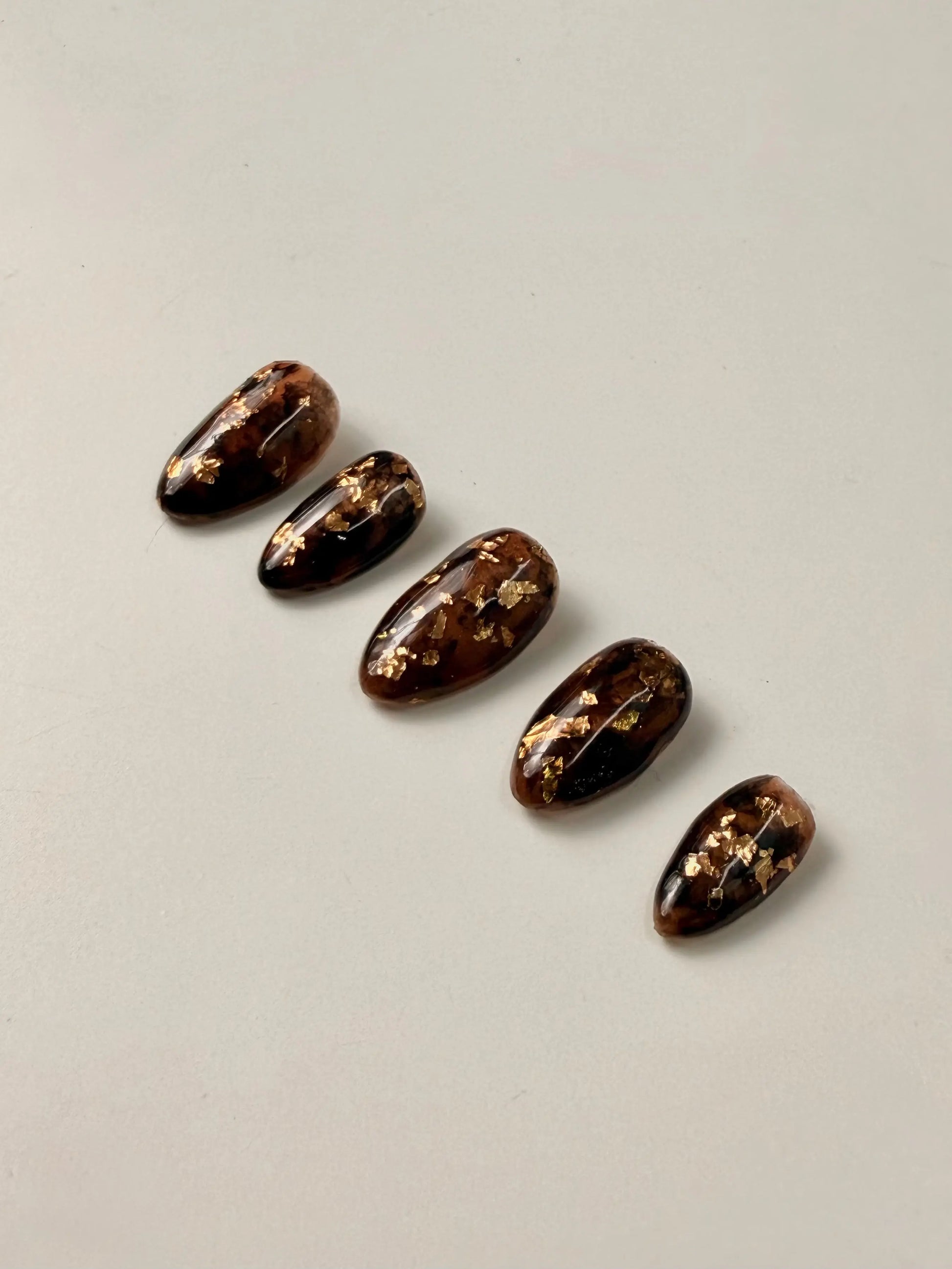 5 press on nails designed in tortoise shell with gold flakes sit in a neat line
