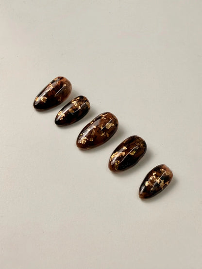 5 press on nails designed in tortoise shell with gold flakes sit in a neat line