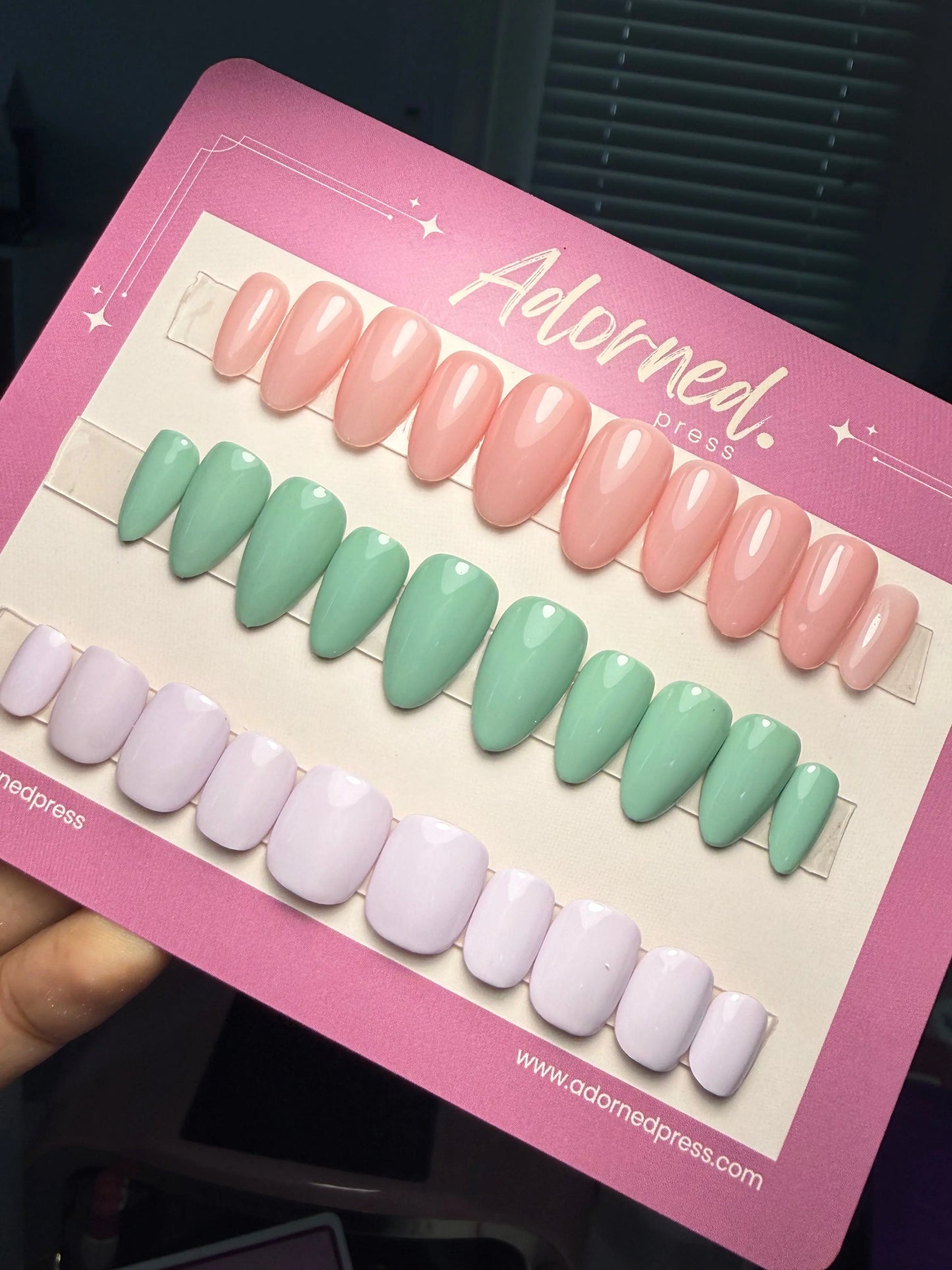 3 sets of press ons in different shapes and colors - pink, pistachio green, and lavender - on a backing card that says Adorned Press